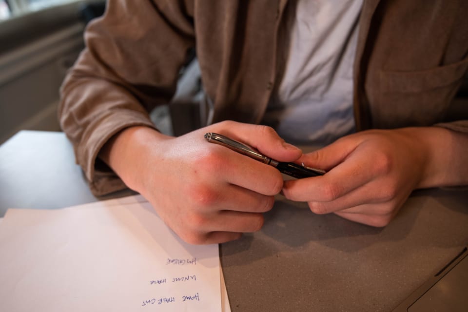 Une personne assise à un bureau tient un stylo au-dessus d'une feuille couverte de notes manuscrites.