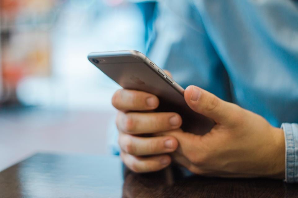 Deux mains tiennent un smartphone au-dessus d'une table en bois sombre, le pouce posé sur l'écran.